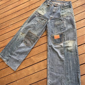 Op de afbeelding: Blauwe denim jeans met meerdere patchwork details en rafelige zoom.