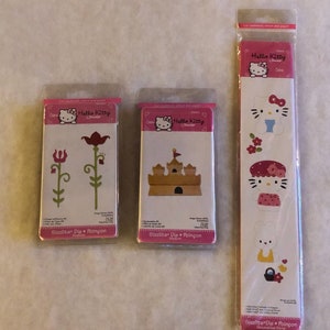 May include: Three packages of Hello Kitty Sizzlits die cuts for crafting. The first package features two flower designs, the second package features a sandcastle design, and the third package features four Hello Kitty designs.