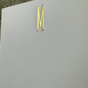 May include: A white card with a gold letter M printed on it.