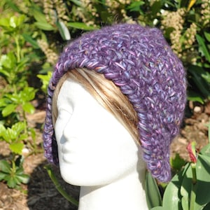 May include: Purple crocheted beanie with a long, pointed brim. The beanie is made with a textured yarn and has a subtle sparkle.