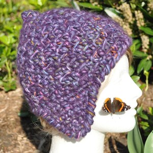 May include: Purple and pink crocheted beanie with a slouchy fit. The beanie is made with a textured stitch and has a unique ear flap design.