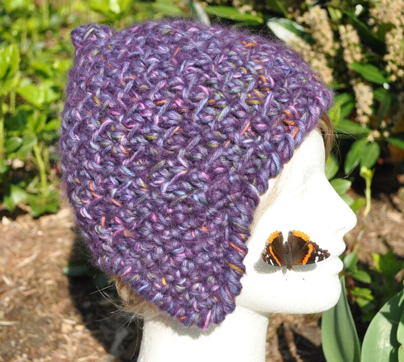 May include: Purple and pink crocheted beanie with a slouchy fit. The beanie is made with a textured stitch and has a unique ear flap design.