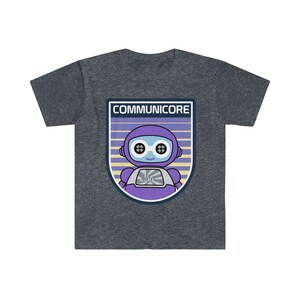 May include: Dark gray t-shirt featuring a purple robot graphic with the text "COMMUNICORE" in a shield design. The robot has blue eyes and a white chest plate. The shirt is made of a soft material.