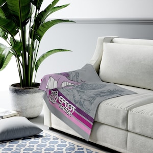 May include: A gray throw blanket with a graphic design featuring the text "EPCOT CENTER" in white and a purple and pink stripe. The blanket is draped over a white couch.