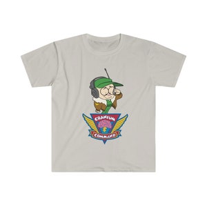 May include: A light grey t-shirt with a cartoon character wearing a green hat and headset. The character is above a colorful emblem that reads "Cranium Command" with a brain graphic. The shirt is made of a soft material.