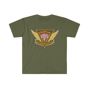 May include: Olive green t-shirt featuring a graphic design. The design includes a pink brain, yellow wings, and the words "Cranium Command" in a vintage style. The shirt is made of a soft, comfortable material.