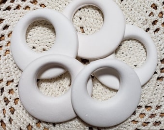 Op de afbeelding: Vijf witte keramische ringen met een glad, afgerond oppervlak en een gat in het midden. De ringen zijn in een cirkel op een wit gehaakt oppervlak gerangschikt.