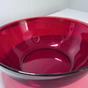 Peut inclure: Un grand saladier rond en verre rouge rubis avec un bord noir. Le bol a une surface lisse et brillante et est vide. Le bol est probablement utilisé pour servir ou pour la présentation.