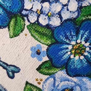May include: Close-up of a floral painting featuring blue and white hydrangeas with green leaves and gold accents. The artwork has a textured, impasto style, with visible brushstrokes. The flowers are the focal point.