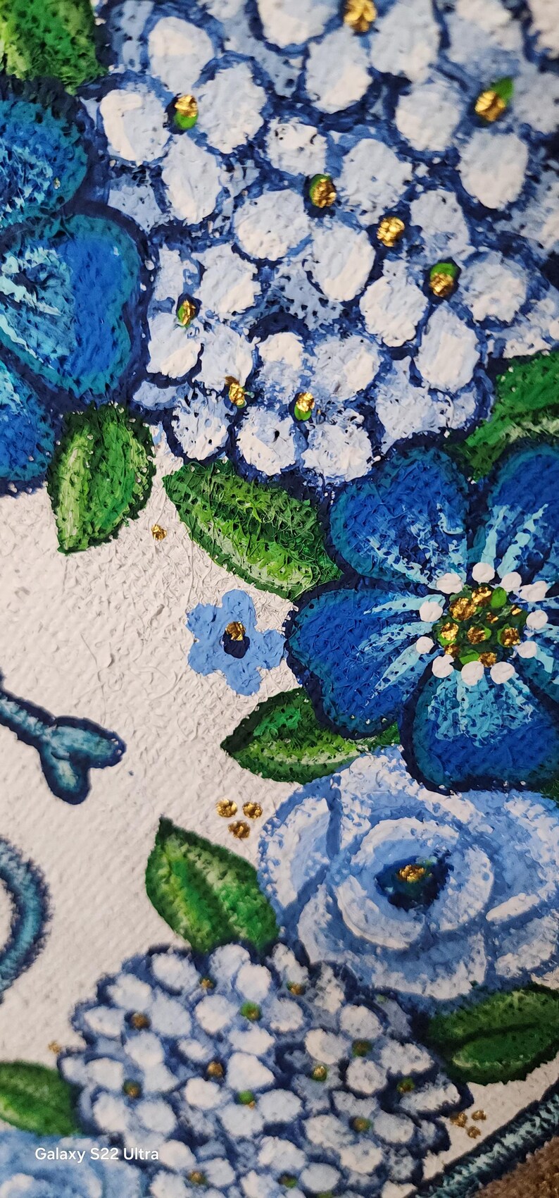 May include: Close-up of a floral painting featuring blue and white hydrangeas with green leaves and gold accents. The artwork has a textured, impasto style, with visible brushstrokes. The flowers are the focal point.