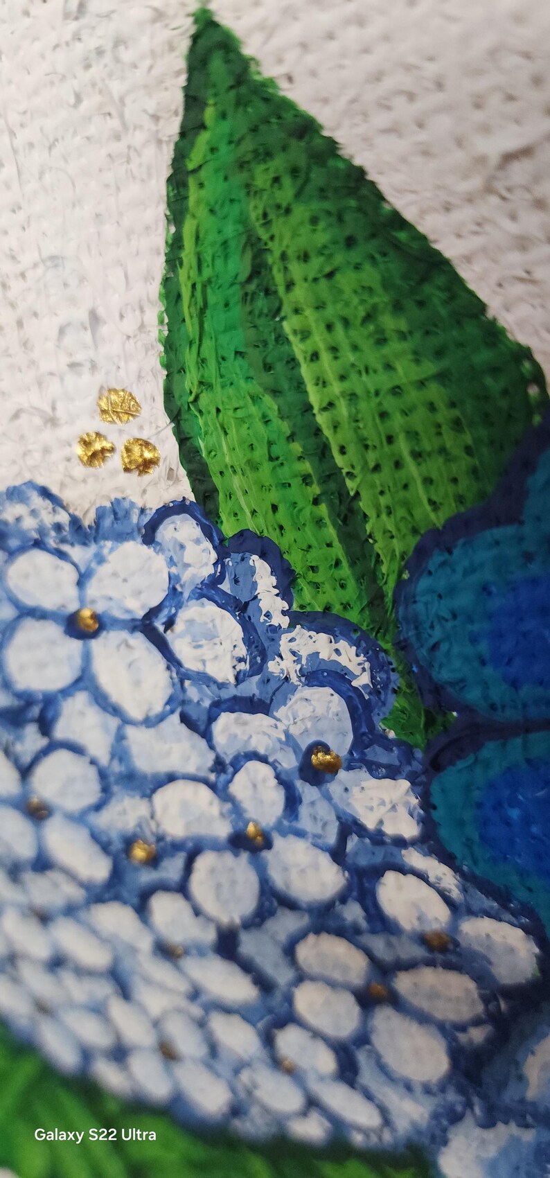 May include: Close-up of a painting featuring blue and white hydrangea flowers with gold accents and a large green leaf. The artwork has a textured, impasto style, with a white background.