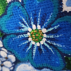 May include: Close-up of a vibrant, textured painting of a blue flower with white accents and a gold centre. The artwork features a textured white background and green leaves, showcasing a floral theme.