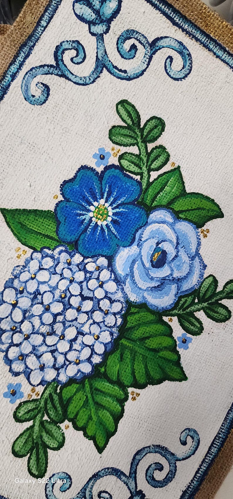 May include: Hand-painted floral artwork featuring blue hydrangeas, roses, and other flowers with green leaves. The painting has a white background and a blue decorative border. Gold accents are scattered throughout the floral arrangement.