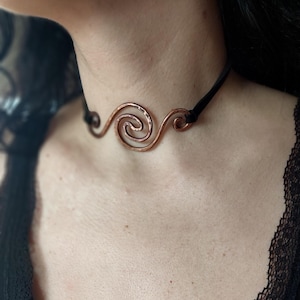 Könnte beinhalten: Eine Kupferdraht-Choker-Halskette mit einem Spiraldesign. Die Kette ist auf einem schwarzen Lederband.