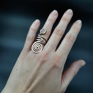 Op de afbeelding: Een zilverkleurige ring met een spiraalvormig ontwerp. De ring wordt gedragen aan de wijsvinger van een hand.
