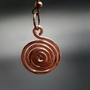 Könnte beinhalten: Ein Kupfer-Spiralenohrring mit einem einfachen Hakenverschluss. Die Spirale besteht aus einem einzigen Draht, der zu einer engen Spirale gedreht ist.