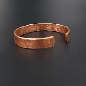 Puede incluir: Una sencilla pulsera de cobre con acabado martillado. La pulsera es de extremo abierto y tiene una forma ligeramente redondeada.