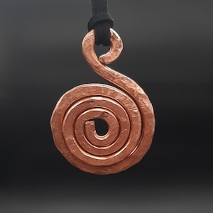 Peut inclure: Un collier avec un pendentif en spirale en cuivre avec une finition martelée. Le pendentif est attaché à un cordon noir.