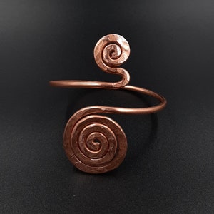 May include: A copper bracelet featuring two hammered spiral designs. The bracelet is open and has a simple, elegant design.