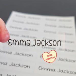 May include: A sheet of rectangular, transparent adhesive labels featuring the name Emma Jackson printed in a black, rounded sans-serif font. The labels are arranged in a grid pattern on a white backing sheet, with one label peeled off.