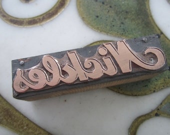 May include: A metal printing block with the word "Wickles" in raised copper letters.