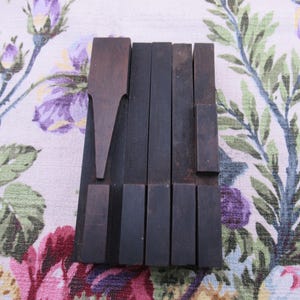 May include: A collection of dark brown, rectangular wooden letterpress blocks arranged in a vertical cluster. The set includes several solid rectangular pieces and one block featuring a distinct triangular, pointed shape at the top end.