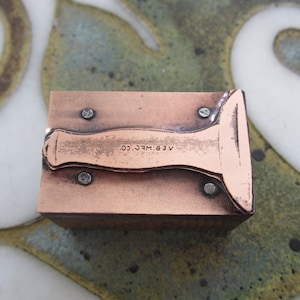 May include: A copper-colored metal stamp with a handle and the text "A.E.B. MFG. CO." on the top.
