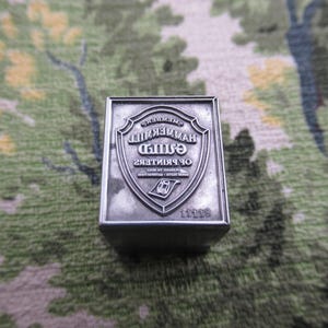 May include: A rectangular silver-toned metal printing block featuring an embossed shield design. The text reads MEMBER HAMMERMILL GUILD OF PRINTERS PLEDGED TO SELL GOOD FAITH SATISFACTION with a small graphic of a printing press and the number 11118.