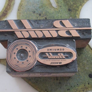 Puede incluir: Un bloque de impresión de metal vintage con la palabra "Bunn" en letras de cobre en relieve. El bloque también presenta un diseño circular con un círculo central y un anillo de círculos más pequeños que lo rodean. El texto "Genuine Cold Tapered Disc Wheel" también es visible en letras de cobre.