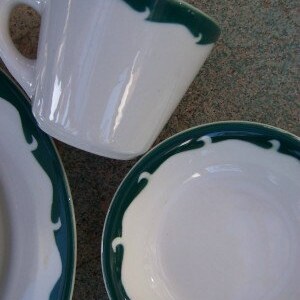 May include: White ceramic teacup and saucer set with a dark green scalloped border design. The teacup has a handle and the saucer is round. The set is clean and simple, suitable for a tea party or daily use.