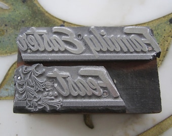Può includere: Due blocchi di stampa in metallo vintage. Un blocco recita "Family Easter" in un carattere script. L'altro blocco recita "Font" con abbellimenti floreali. Entrambi i blocchi sono montati su una base di legno scuro.