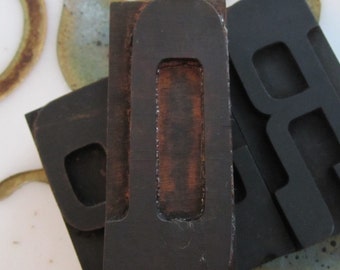 May include: Close-up of a wooden letterpress block with the letter "O" carved into it. The block is dark brown and has a worn, vintage look.