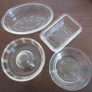 Puede incluir: Un conjunto de cuatro platos de vidrio transparente de diversas formas y tamaños. El set incluye un plato ovalado, uno rectangular y dos circulares, todos con patrones moldeados en la base y los laterales que les dan una apariencia texturizada.