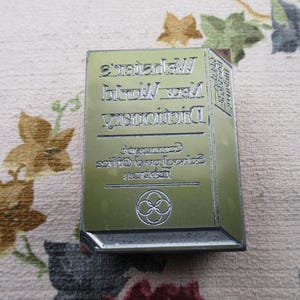 Puede incluir: Una taza de cerámica blanca con un asa negra y el texto "But First, Coffee" en negro, con una fuente de estilo manuscrito. La taza está sobre una superficie blanca.