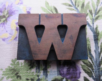 May include: A vintage wooden letterpress block featuring the letter "W". The block is made of brown wood with a dark blue base and interior accents. The letter has a unique, aged appearance, perfect for printing or display.