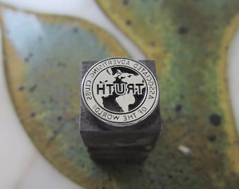 May include: A silver metal stamp with a circular design. The design features a globe with the word "TRUTH" printed in bold letters. The text around the globe reads "Associated Advertising Clubs of the World".