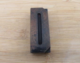 May include: A vintage wooden letterpress printing block of the letter "I". The block is rectangular with a deep, narrow channel forming the letter. The wood has a dark, aged appearance with visible grain and wear.