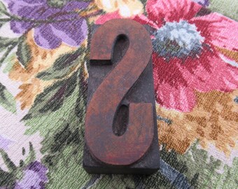May include: A wooden letterpress block in the shape of the number 8. The block is brown and has a worn, rustic look. It is sitting on a floral fabric background.