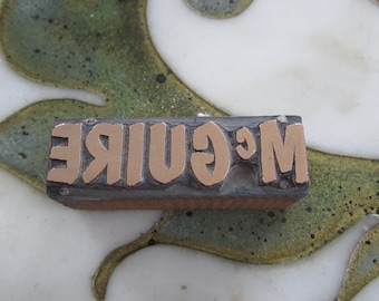 May include: A vintage wood printing block with the word "McGuire" in raised gold letters.