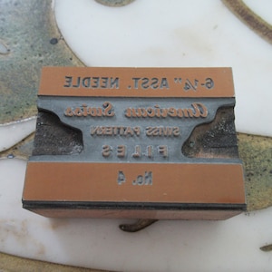 Può includere: Un blocco di legno marrone con una piastra metallica su cui è scritto "No. 4 Files Swiss Pattern American Swiss 6-1/2" ASS'T. NEEDLE".