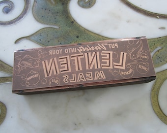 May include: A vintage brown wooden printing block with the text "MEALS LEITEN PUT Variety INTO YOUR" and images of fish, eggs, macaroni, cheese, and soup.