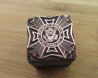 Puede incluir: Un sello de metal de color cobre con la inscripción "Veterans of Foreign Wars of the United States" y un diseño de águila estilizado.