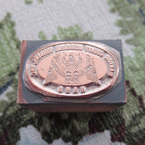 May include: A close-up of a metal stamp with an oval design. The design features an eagle with its wings spread, surrounded by the text "NATION COUNTY RESIDENTIAL BUILDERS INC."