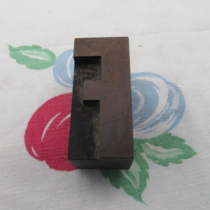 May include: A wooden letter F printing block. The block is dark brown with a black border. The letter F is carved into the block.