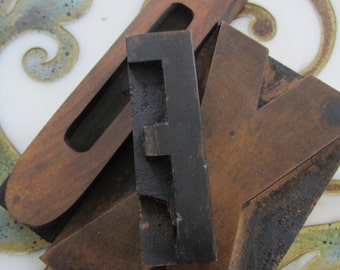 Könnte beinhalten: Drei Holz-Letterpress-Blöcke, einer mit dem Buchstaben "F" in schwarzer Farbe, einer mit dem Buchstaben "V" in brauner Farbe und einer mit dem Buchstaben "O" in brauner Farbe.