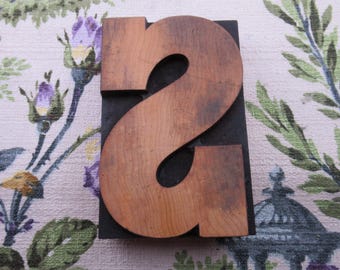 May include: A vintage wooden letterpress number two. The number is made of light brown wood with a dark grain and is mounted on a black base. The number is a classic serif font.