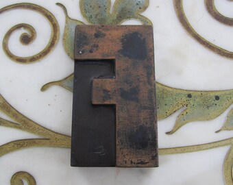 Puede incluir: Un bloque de impresión de madera vintage en forma de letra F con un acabado marrón oscuro y cobre. El bloque tiene un aspecto desgastado y envejecido, con signos visibles de uso.