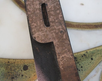 May include: A wooden letterpress block with the letter "P" carved into it. The block is made of dark wood with a brown, worn surface.