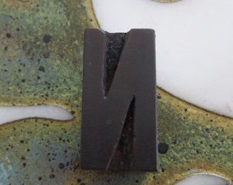 May include: A dark brown wooden letter N, with a slightly rough texture, is displayed against a background of green, blue, and gold swirls.