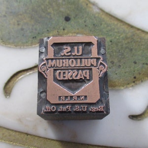Puede incluir: Un bloque de impresión de metal vintage con una inscripción de color cobre que dice "Reg. U.S. Pat. Off. N.P.L. PASSED PULLORUM U.S."